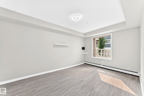 Recessed ceiling light, tray ceiling, wood-finish flooring, white trim, and a wall-mounted shelf - #137 9704 174 St Nw, Edmonton, AB - Indoor Photo Showing Other Room
