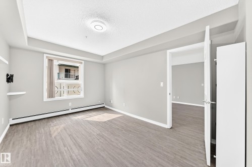 Wood-finish flooring, contemporary ceiling light fixture, white trim, and a window with a white frame - #137 9704 174 St Nw, Edmonton, AB - Indoor Photo Showing Other Room