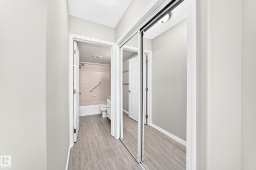Hallway featuring light wood-finish flooring, white trim, and a mirrored closet with sliding doors - #137 9704 174 St Nw, Edmonton, AB - Indoor Photo Showing Other Room