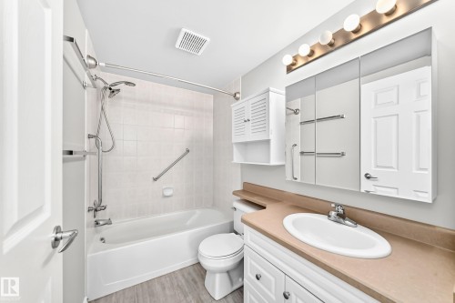 White vanity with dual cabinet storage, an integrated sink, and a light-toned countertop - #137 9704 174 St Nw, Edmonton, AB - Indoor Photo Showing Bathroom