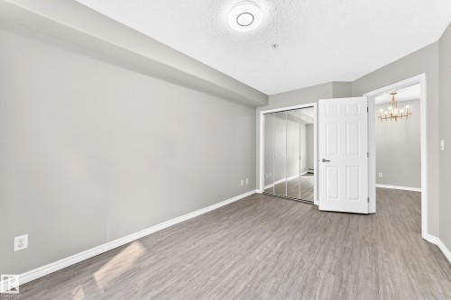 Wood-finish flooring, mirrored sliding closet doors, ceiling-mounted light fixture, paneled interior door, and an overhead chandelier in an adjoining room - #137 9704 174 St Nw, Edmonton, AB - Indoor Photo Showing Other Room