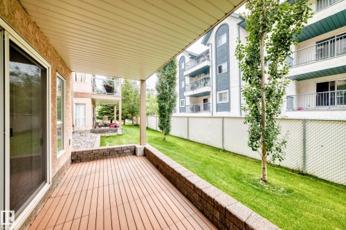 Covered patio featuring wood-finish decking and a low stone wall - #137 9704 174 St Nw, Edmonton, AB - Outdoor With Exterior