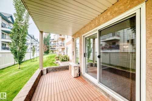 Covered patio with wood-finish decking and stone retaining wall - #137 9704 174 St Nw, Edmonton, AB - Outdoor With Exterior