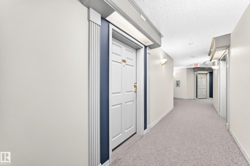 Wall-mounted sconce lighting illuminates the neutral-toned walls and light-colored carpeted flooring, creating a bright corridor - #137 9704 174 St Nw, Edmonton, AB - Indoor Photo Showing Other Room