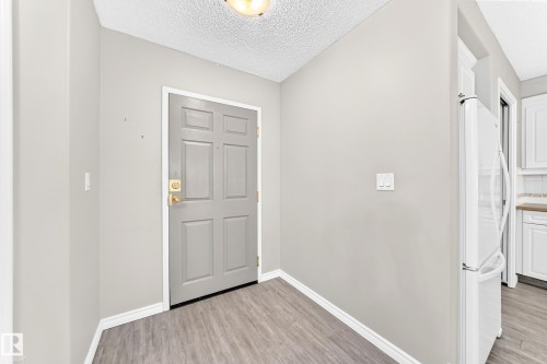 Wood-finish flooring, light gray interior walls, and a paneled entry door with brass hardware - #137 9704 174 St Nw, Edmonton, AB - Indoor Photo Showing Other Room