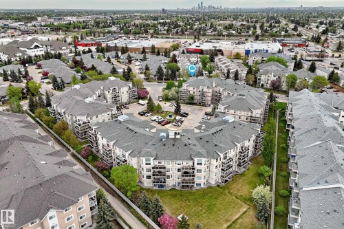 Aerial view of a modern multi-unit residential complex featuring curved architectural design, manicured landscaping with mature trees, and integrated green space - #137 9704 174 St Nw, Edmonton, AB - Outdoor With View