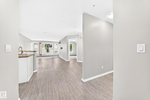 Wood-finish flooring throughout, light gray wall paint, white trim, recessed lighting, and large windows with white frames - #137 9704 174 St Nw, Edmonton, AB - Indoor Photo Showing Other Room