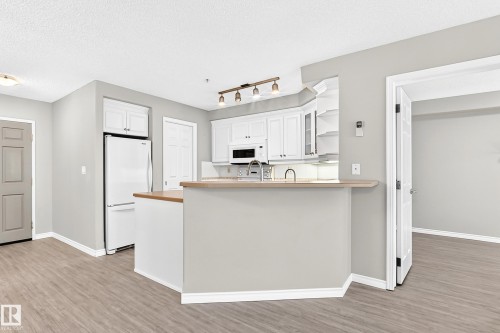 Kitchen with white cabinetry, wood-finish countertops, stainless steel sink, and track lighting - #137 9704 174 St Nw, Edmonton, AB - Indoor Photo Showing Kitchen