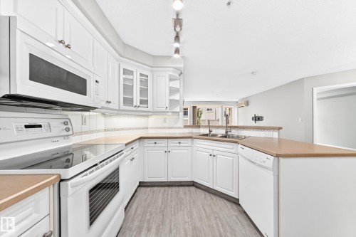 White cabinetry, light wood-finish flooring, built-in microwave, integrated dishwasher, and a double basin sink - #137 9704 174 St Nw, Edmonton, AB - Indoor Photo Showing Kitchen With Double Sink