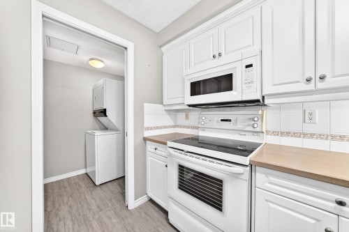 White cabinetry, stainless steel microwave, electric range, tiled backsplash, and wood-finish countertops - #137 9704 174 St Nw, Edmonton, AB - Indoor Photo Showing Kitchen
