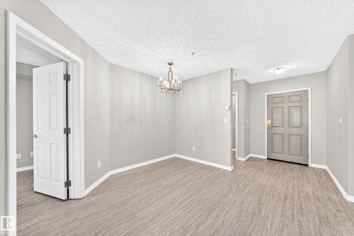 Wood-finish flooring throughout, light gray wall paint, white trim, brass-finish chandelier - #137 9704 174 St Nw, Edmonton, AB - Indoor Photo Showing Other Room