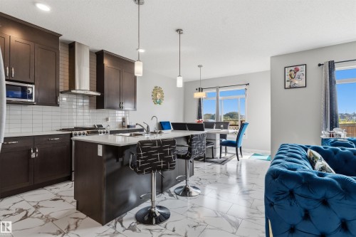 Open-concept kitchen with dark wood cabinetry, white subway tile backsplash, stainless steel appliances, and a central island with a white countertop - 1103 26 Avenue Nw, Edmonton, AB - Indoor Photo Showing Kitchen With Upgraded Kitchen