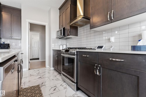 Dark wood-finish cabinetry, stainless steel appliances, white subway tile backsplash, light-toned countertops, and marble-look floor tiling - 1103 26 Avenue Nw, Edmonton, AB - Indoor Photo Showing Kitchen With Upgraded Kitchen