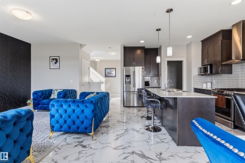 Open-concept interior featuring large format marble-look tile flooring, a kitchen island with seating, dark wood-finish cabinetry, and stainless steel appliances - 1103 26 Avenue Nw, Edmonton, AB - Indoor Photo Showing Kitchen With Upgraded Kitchen