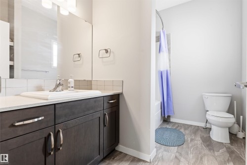 Wood-finish flooring, dark wood-tone vanity with chrome hardware, white countertop with integrated sink, white subway tile backsplash, and a built-in tub with shower - 1103 26 Avenue Nw, Edmonton, AB - Indoor Photo Showing Bathroom