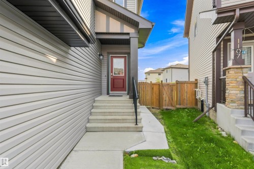 Red entry door, concrete steps with black handrail, light-colored horizontal siding, and a wood privacy fence - 1103 26 Avenue Nw, Edmonton, AB - Outdoor With Exterior