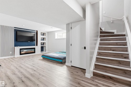 Recessed media wall with electric fireplace and integrated shelving, light wood-finish flooring, white painted staircase with wood-finish treads, white interior door with matte black hardware, and an egress window - 1103 26 Avenue Nw, Edmonton, AB - Indoor With Fireplace