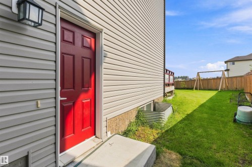 Red paneled exterior door with an overhead lantern fixture, siding exterior, and a backyard with a swing set - 1103 26 Avenue Nw, Edmonton, AB - Outdoor With Exterior