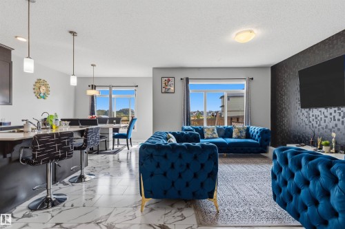 Open-concept living area featuring a kitchen island with seating, pendant lighting, large windows, and a textured accent wall - 1103 26 Avenue Nw, Edmonton, AB - Indoor Photo Showing Living Room