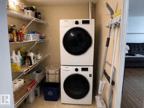 Built-in wire shelving, stacked front-load laundry appliances, and tile flooring - #301 13907 136 St Nw, Edmonton, AB - Indoor Photo Showing Laundry Room