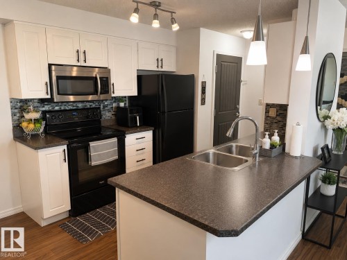 Kitchen featuring white cabinetry, dark countertops, stainless steel appliances, and a mosaic tile backsplash - #301 13907 136 St Nw, Edmonton, AB - Indoor Photo Showing Kitchen With Double Sink