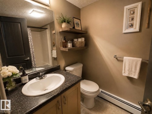 Vanity with an integrated sink, dark speckled countertop, and wood-finish cabinetry - #301 13907 136 St Nw, Edmonton, AB - Indoor Photo Showing Bathroom