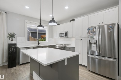 Kitchen featuring white shaker-style cabinetry, a contrasting island with a solid surface countertop, stainless steel appliances, a white subway tile backsplash, and wood-finish flooring - 7603 Summerside Grande Boulevard Sw, Edmonton, AB - Indoor Photo Showing Kitchen With Upgraded Kitchen