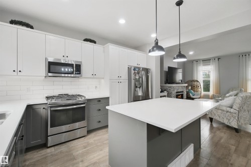 Kitchen featuring white cabinetry with dark hardware, a white subway tile backsplash, stainless steel appliances, and a central island with a white countertop - 7603 Summerside Grande Boulevard Sw, Edmonton, AB - Indoor Photo Showing Kitchen With Double Sink With Upgraded Kitchen