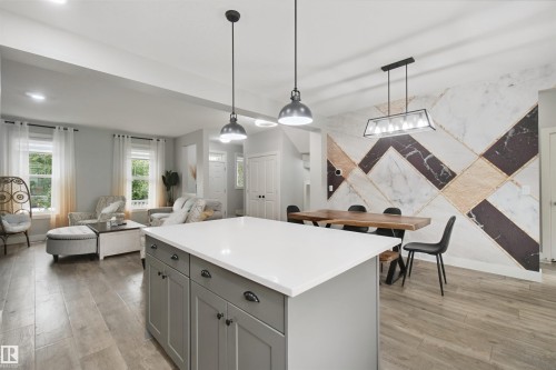 Kitchen island with a white countertop and gray cabinetry, wood-finish flooring, geometric accent wall, and pendant lighting - 7603 Summerside Grande Boulevard Sw, Edmonton, AB - Indoor