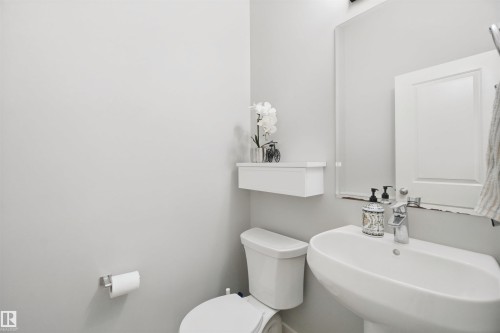Pedestal sink with chrome-finish faucet, wall-mounted mirror, and white toilet - 7603 Summerside Grande Boulevard Sw, Edmonton, AB - Indoor Photo Showing Bathroom