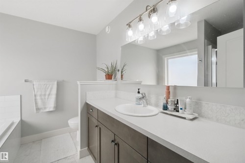 Extended vanity with integrated sink, brushed nickel lighting fixture, large vanity mirror, white subway tile tub surround, and white tile flooring - 7603 Summerside Grande Boulevard Sw, Edmonton, AB - Indoor Photo Showing Bathroom