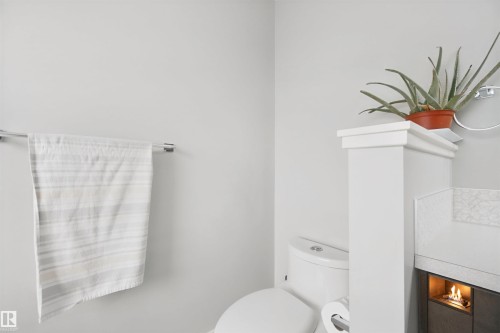 White toilet with a built-in privacy wall, featuring a decorative top ledge and an integrated fireplace - 7603 Summerside Grande Boulevard Sw, Edmonton, AB - Indoor Photo Showing Bathroom
