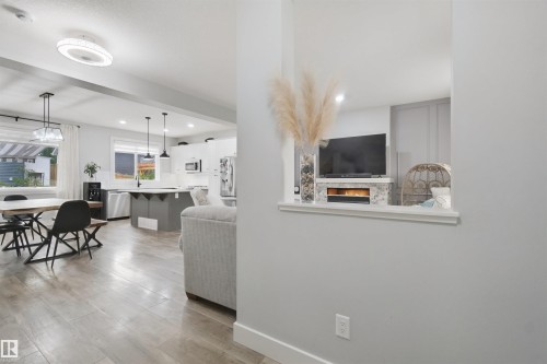 Open-concept living space with wood-finish flooring, a contemporary ceiling light fixture, a kitchen island with pendant lighting, and a built-in electric fireplace - 7603 Summerside Grande Boulevard Sw, Edmonton, AB - Indoor