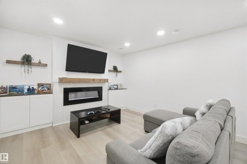 Contemporary living space featuring an electric fireplace with a hexagon tile surround, wood-finish flooring, recessed lighting, and built-in cabinetry - 7603 Summerside Grande Boulevard Sw, Edmonton, AB - Indoor With Fireplace