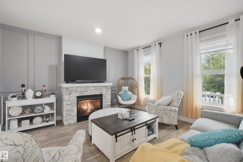 Fireplace with stone surround, wood-finish flooring, recessed lighting, and wall paneling - 7603 Summerside Grande Boulevard Sw, Edmonton, AB - Indoor Photo Showing Living Room With Fireplace