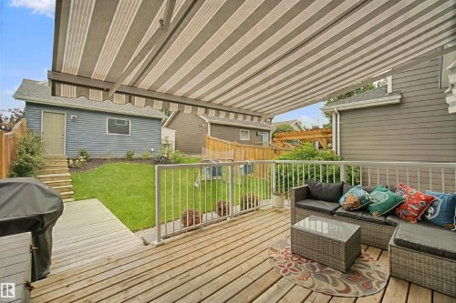 Expansive wood-plank deck with a retractable striped awning, white railings, and a manicured lawn - 7603 Summerside Grande Boulevard Sw, Edmonton, AB - Outdoor With Deck Patio Veranda With Exterior