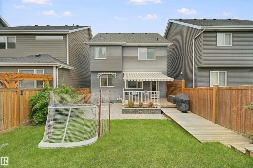 Manicured lawn, elevated deck with awning, wooden privacy fencing, gravel hardscaping, and a sloped wooden walkway - 7603 Summerside Grande Boulevard Sw, Edmonton, AB - Outdoor With Exterior