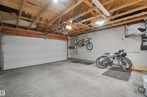 Attached garage with a wide white overhead door, exposed wood ceiling beams, and concrete flooring - 7603 Summerside Grande Boulevard Sw, Edmonton, AB - Indoor Photo Showing Garage
