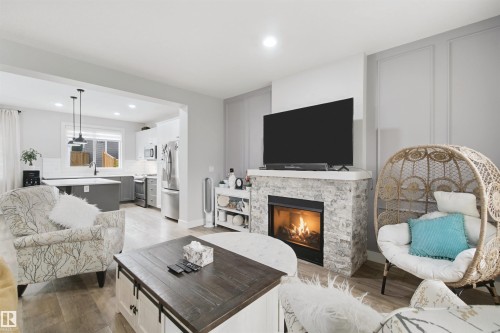 Living area with a stone-clad fireplace and light-toned wood-finish flooring - 7603 Summerside Grande Boulevard Sw, Edmonton, AB - Indoor Photo Showing Living Room With Fireplace