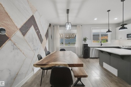 Geometric accent wall, wood-finish flooring, white kitchen cabinetry, stainless steel appliances, and pendant lighting fixtures - 7603 Summerside Grande Boulevard Sw, Edmonton, AB - Indoor