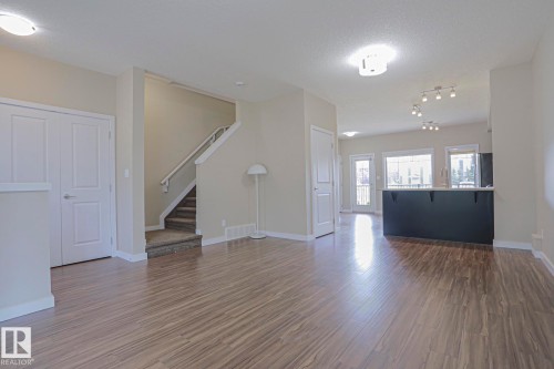 Wood-finish flooring, staircase with carpeted treads, white two-panel doors, and built-in breakfast bar with pendant lighting - #13 5873 Mullen Pl Nw, Edmonton, AB - Indoor Photo Showing Other Room