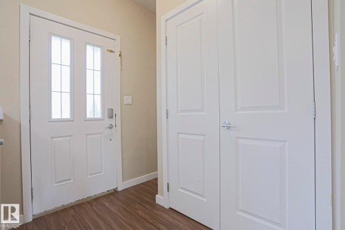 Entryway with a white paneled door featuring decorative glass inserts, a smart lock system, and wood-finish flooring - #13 5873 Mullen Pl Nw, Edmonton, AB - Indoor Photo Showing Other Room