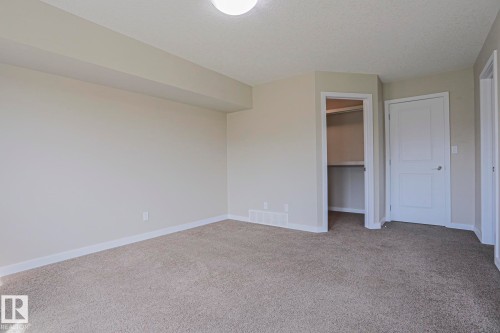 Carpeted flooring, neutral wall paint, overhead lighting, white trim, and a built-in closet with shelving - #13 5873 Mullen Pl Nw, Edmonton, AB - Indoor Photo Showing Other Room