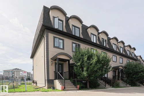 Stucco exterior with dark trim accents, gabled roofline with dormer windows, covered entryways, and concrete steps with dark railings - #13 5873 Mullen Pl Nw, Edmonton, AB - Outdoor With Facade