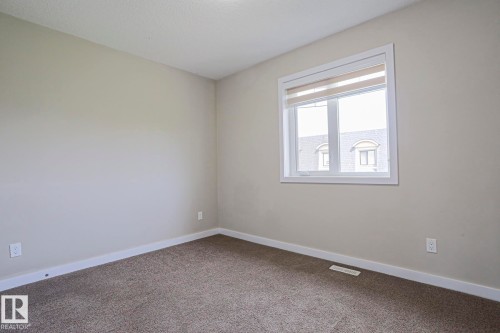 Beige interior walls with a single window featuring white trim and roller shades - #13 5873 Mullen Pl Nw, Edmonton, AB - Indoor Photo Showing Other Room