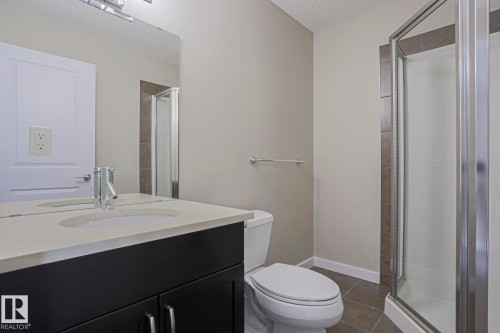 Dark wood-finish vanity with an integrated sink, polished chrome faucet, rectangular mirror, and an enclosed shower with glass panels - #13 5873 Mullen Pl Nw, Edmonton, AB - Indoor Photo Showing Bathroom