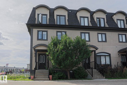 Stucco exterior with a mansard roofline and multiple dormer windows - #13 5873 Mullen Pl Nw, Edmonton, AB - Outdoor With Facade