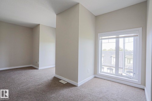 Neutral wall paint, plush carpet flooring, white trim, and a large casement window with white framing - #13 5873 Mullen Pl Nw, Edmonton, AB - Indoor Photo Showing Other Room