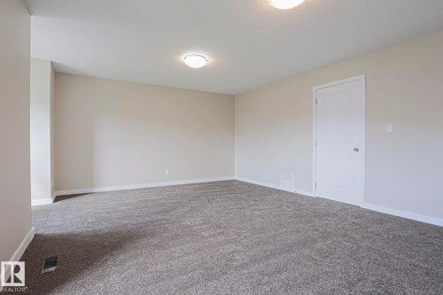 Spacious room featuring neutral carpeting, light-toned walls, and a white panel door - #13 5873 Mullen Pl Nw, Edmonton, AB - Indoor Photo Showing Other Room