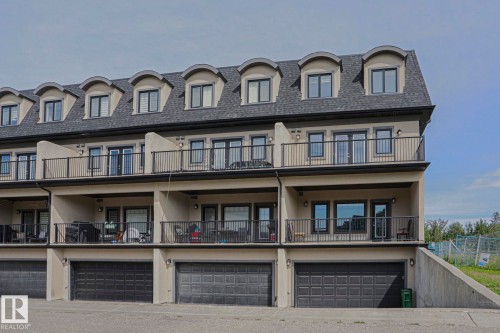 Multi-level townhome exterior featuring dormer windows, private balconies with black railings, ground-level patios, and individual garage access - #13 5873 Mullen Pl Nw, Edmonton, AB - Outdoor With Balcony With Facade
